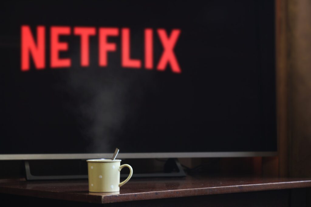 The photo shows a mug with a spoon sitting in it in front of a TV. The TV has the Netflix logo on it. The mug is in focus, and the TV is not. 